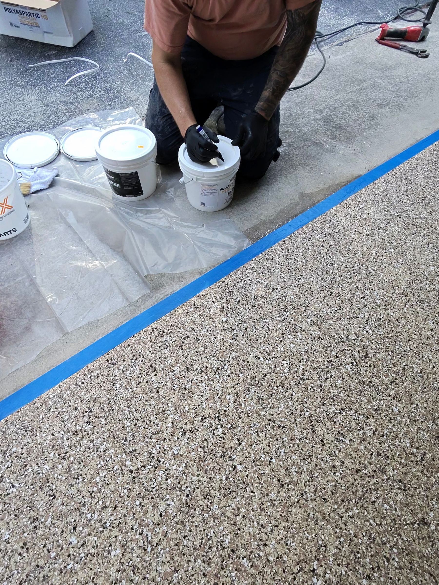 Installer kneeling beside a finished section of flake floor with coating buckets and materials