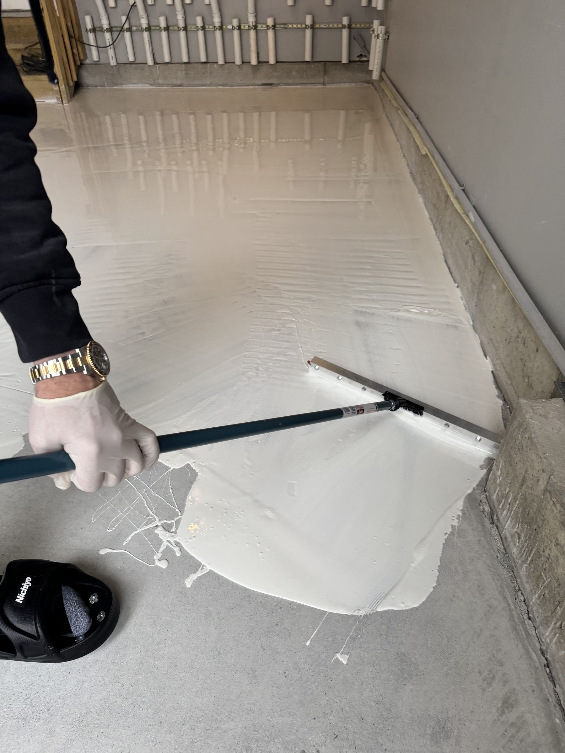 Gloved hand spreading a white epoxy coat across the ground garage slab with a squeegee
