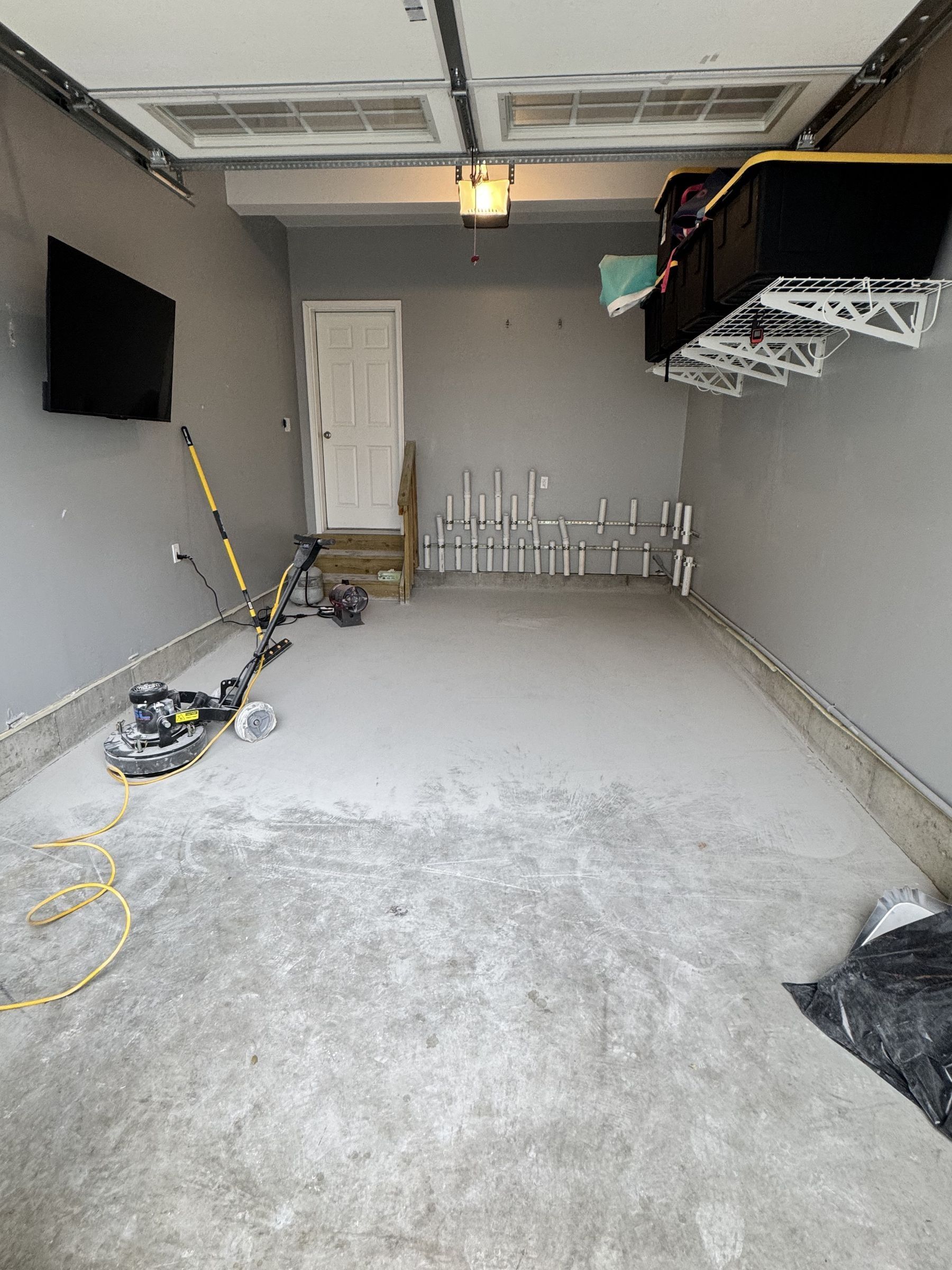 One-car garage with the bare concrete slab being ground, floor grinder and vacuum on the slab