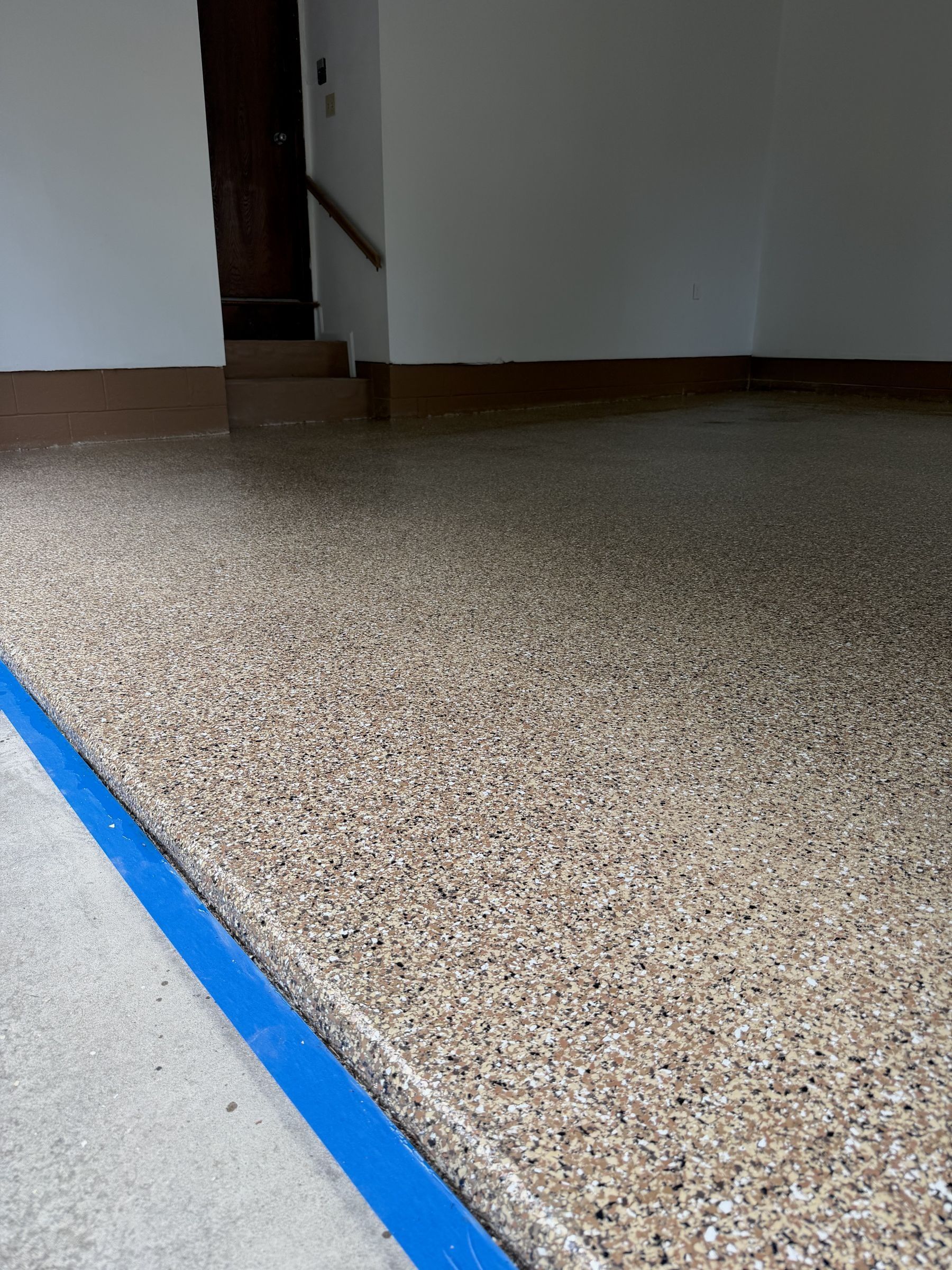 Finished tan, black and white flake epoxy garage floor with a taped edge at the door